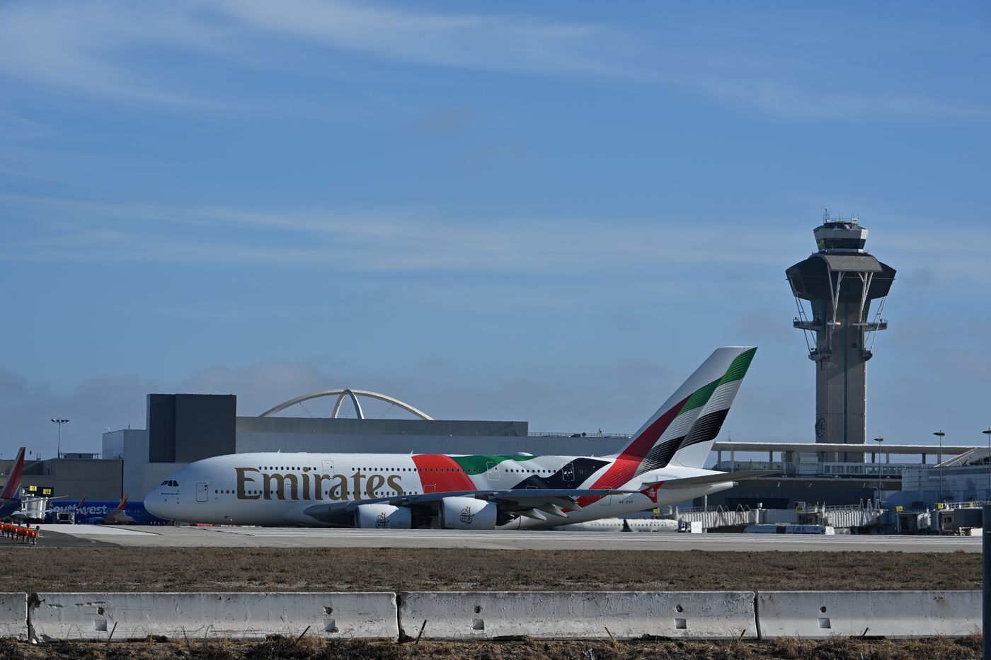 A wide-body airliner at the terminal at LAX with the control tower behind it